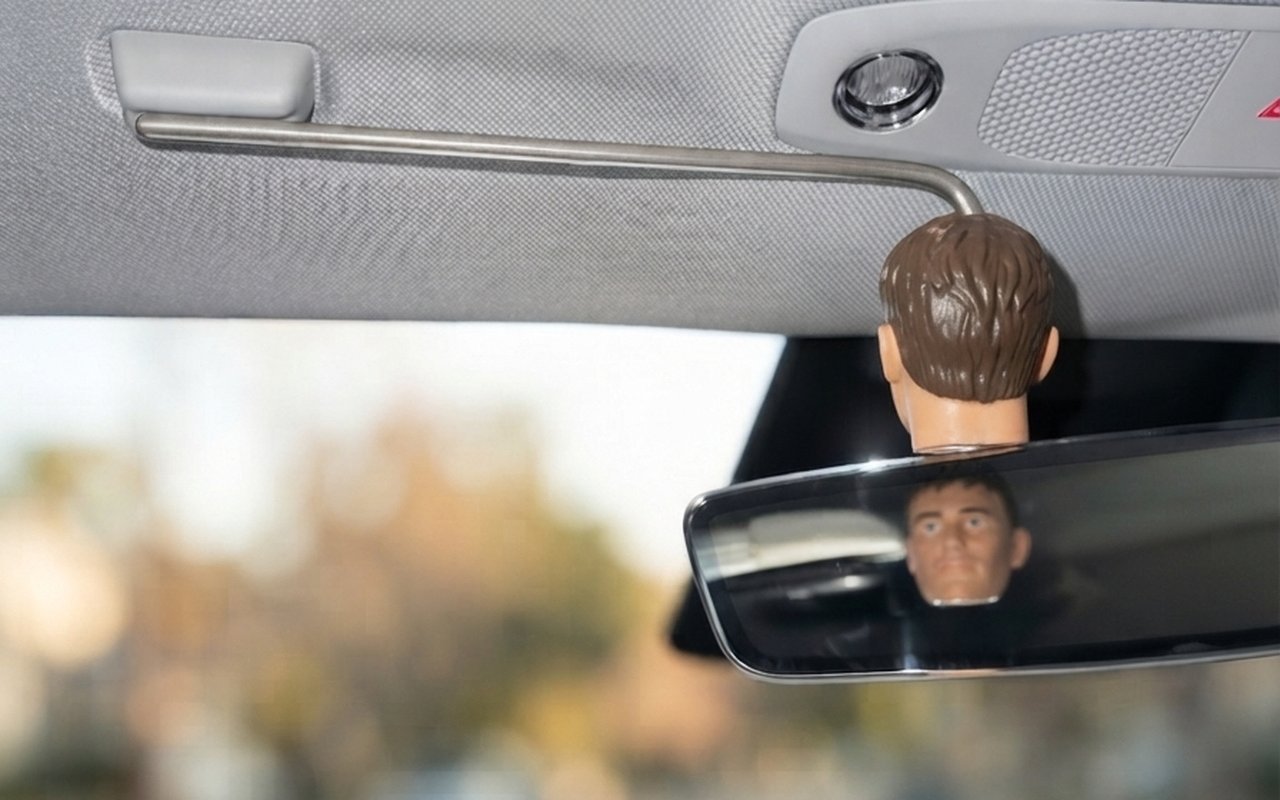 CO·PILOT attached to the visor magnet inside a Tesla, head hanging beside the rearview mirror